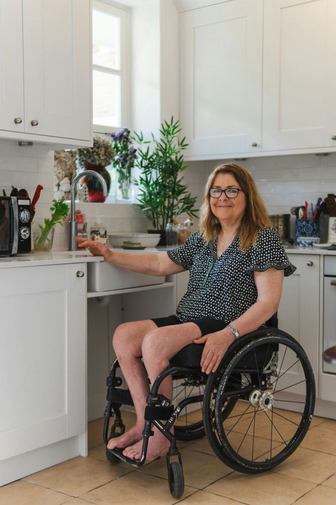 A woman using a wheelchair prepares food at a kitchen bench set at a comfortable height.